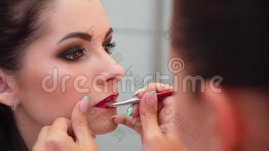 化妆师描绘了年轻女孩的嘴<strong>唇</strong>。 用刷子涂你的嘴<strong>唇</strong>。 红色。 化妆师化妆